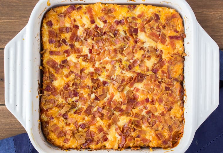 A Baked Keto Breakfast Casserole in a white square baking dish on a wood background with a dark blue napkin
