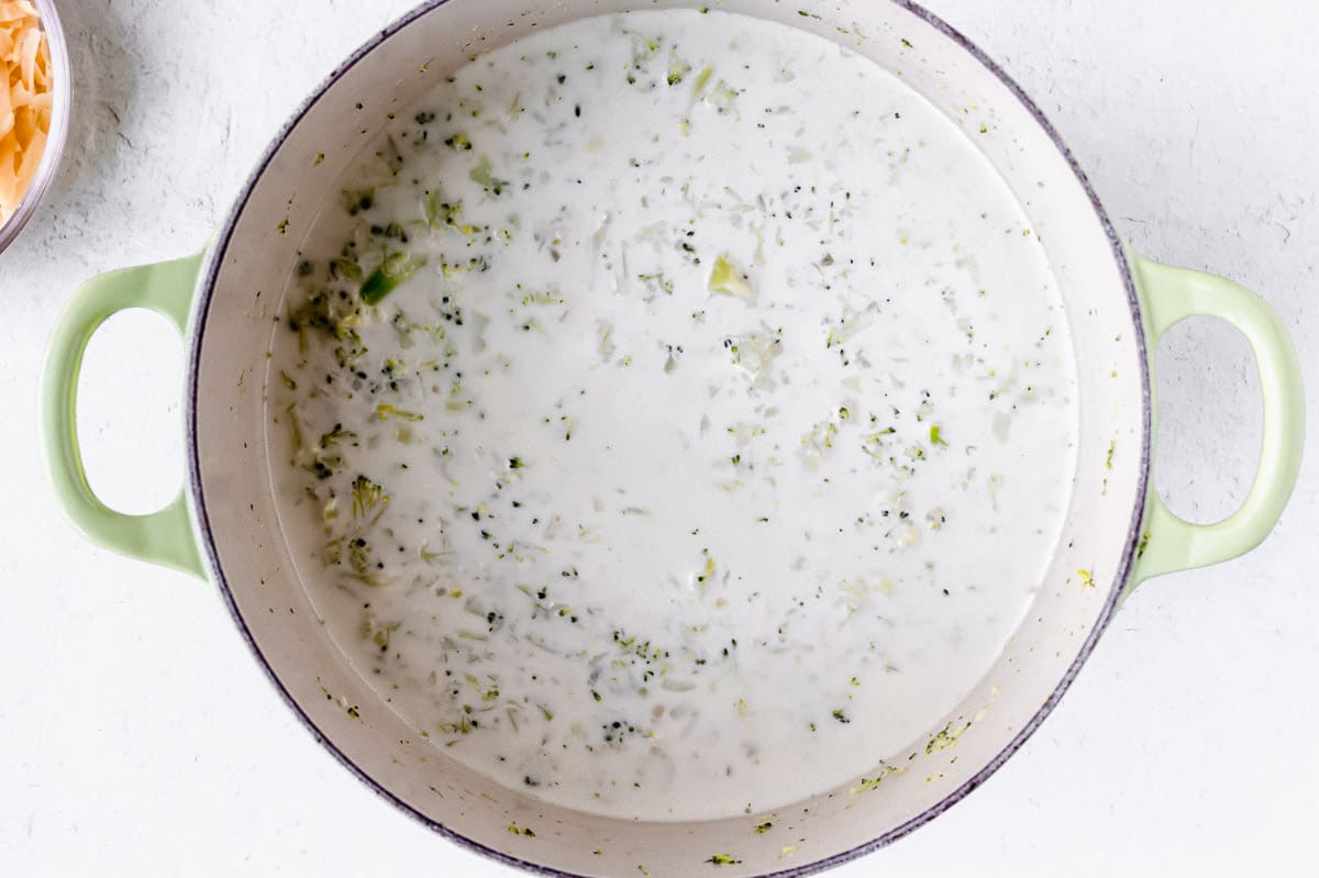 Broccoli soup with added cream cooking in a Dutch oven over a white background