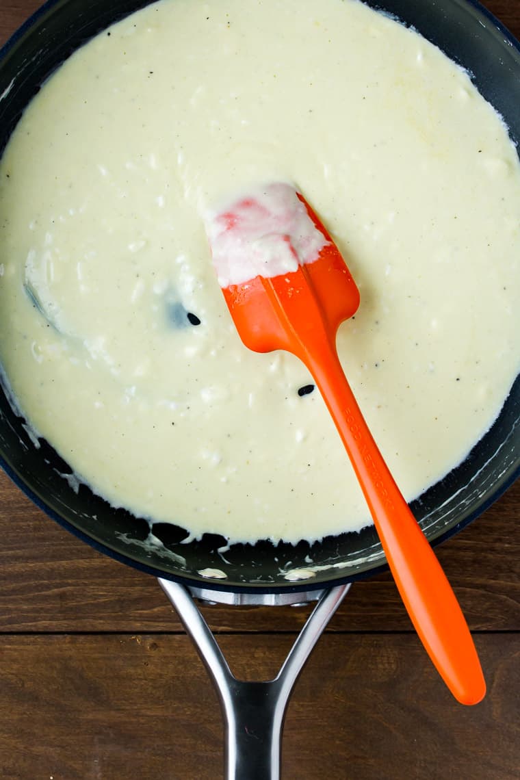 Cream cheese and butter melted in a black skillet with an orange spatula on a wood backdrop