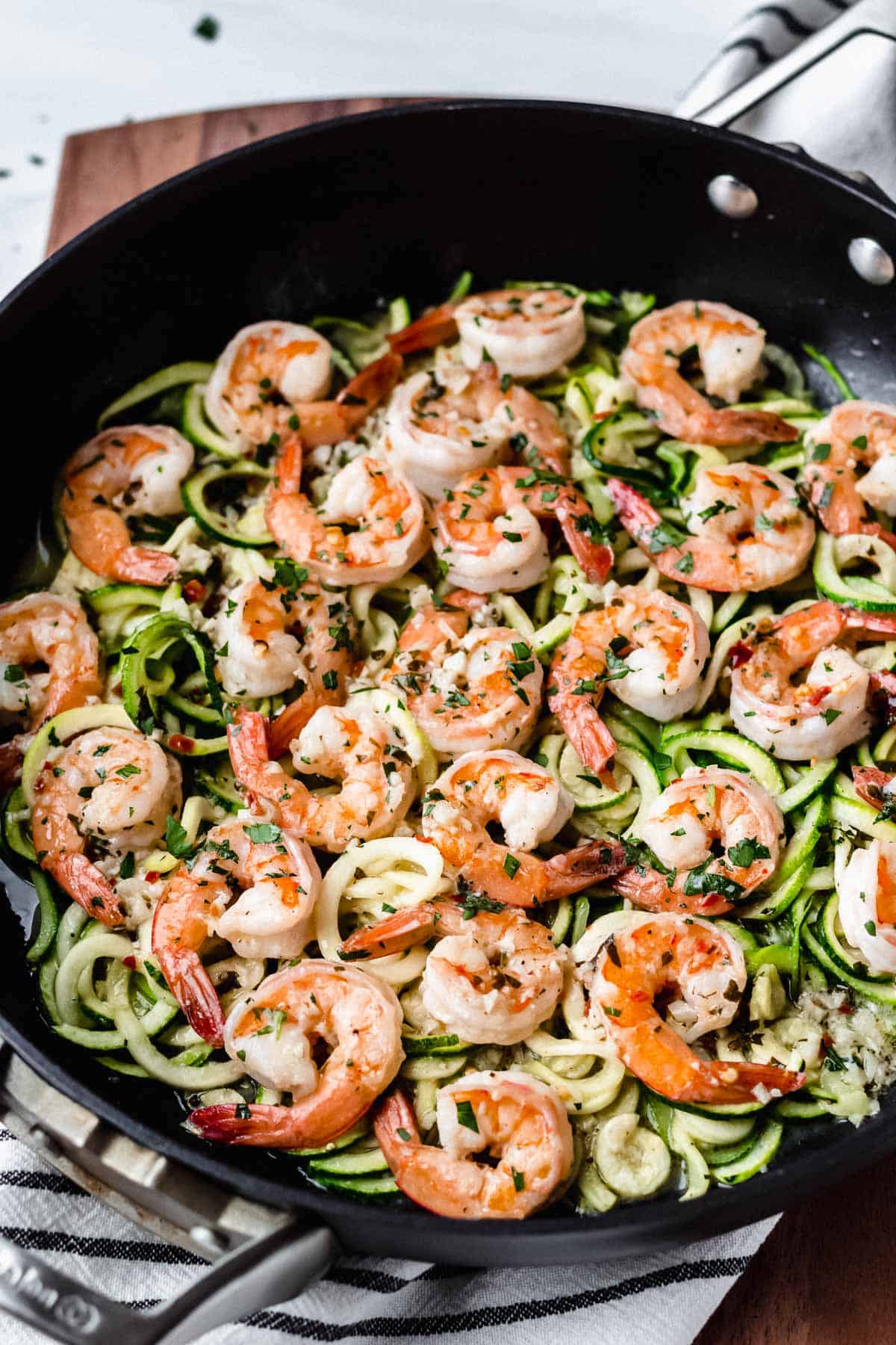 Skillet with Keto Shrimp Scampi and zoodles on a white striped towel on a wood background