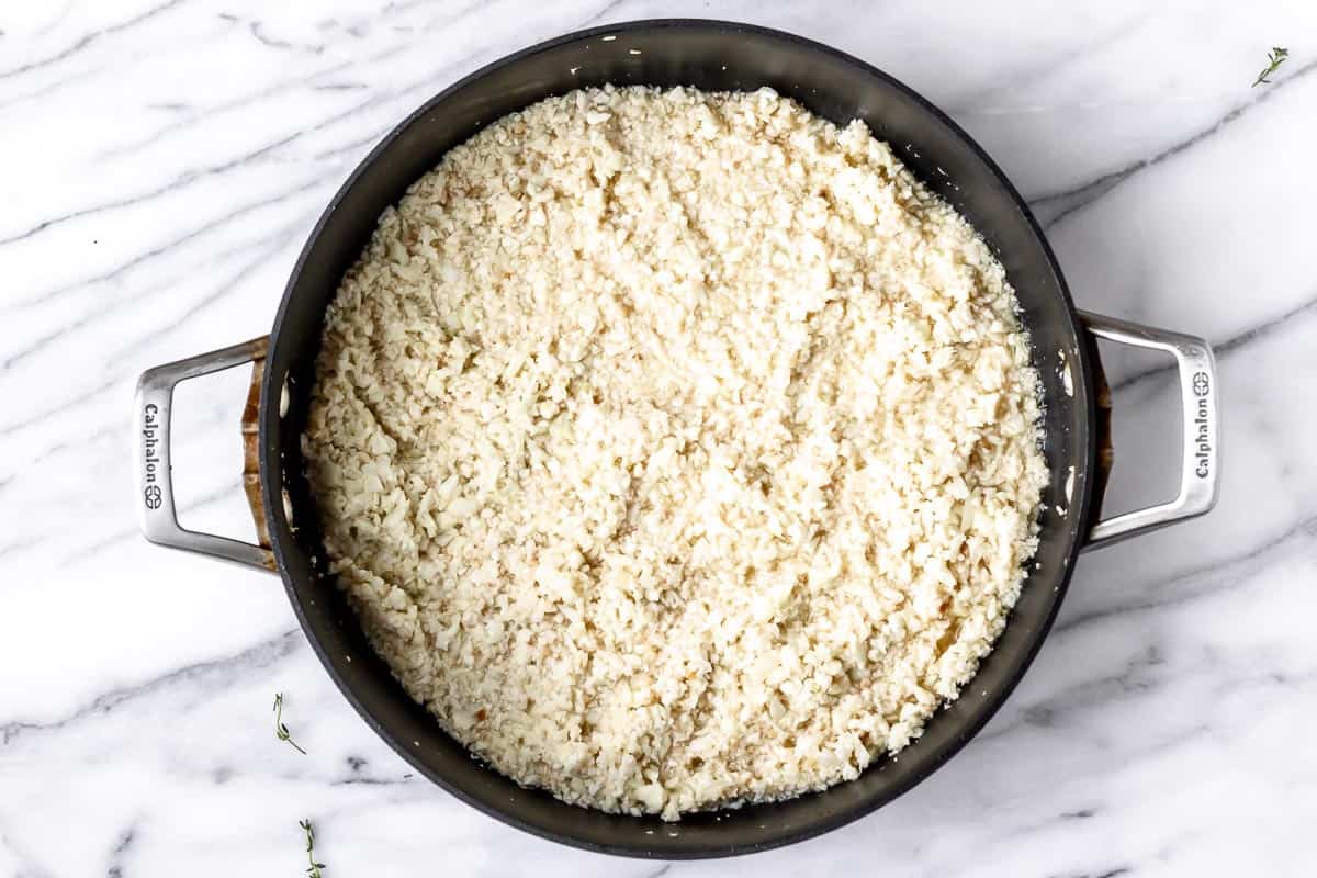 Cooked cauliflower rice in a black skillet.