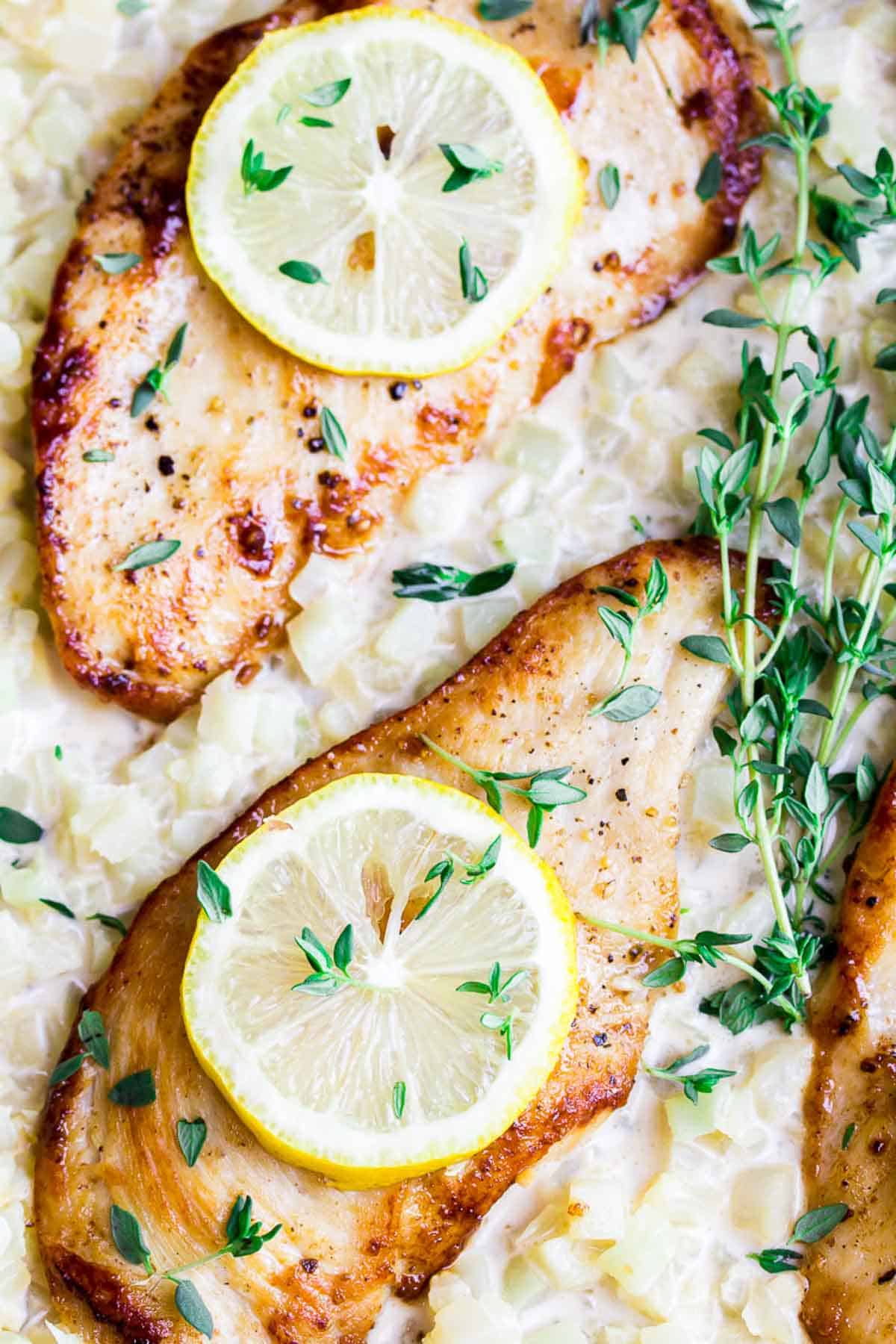 Close up at two lemon chicken breasts topped with lemon slices and thyme.