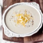 White cheddar cauliflower soup in a white bowl on a wood board