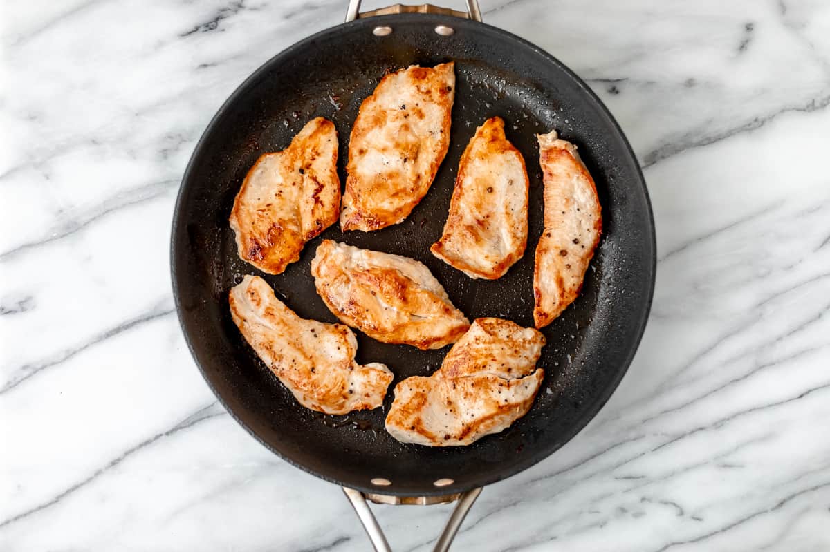 Seven small chicken breasts cooked in a black skillet.