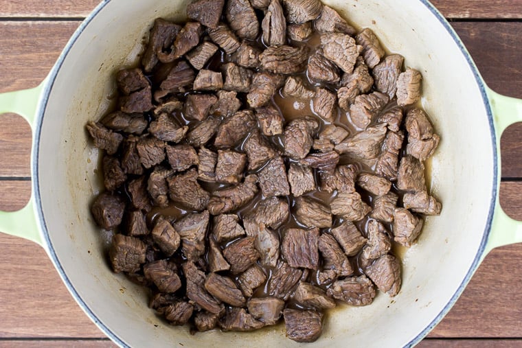 Bite-size pieces of steak cooking in a pot on a wood background