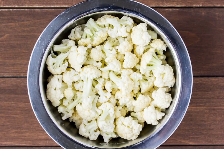 Overhead view of cauliflower florets in a silver bowl over a wood background
