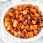 A white bowl full of maple bacon sweet potato hash on a marble table.