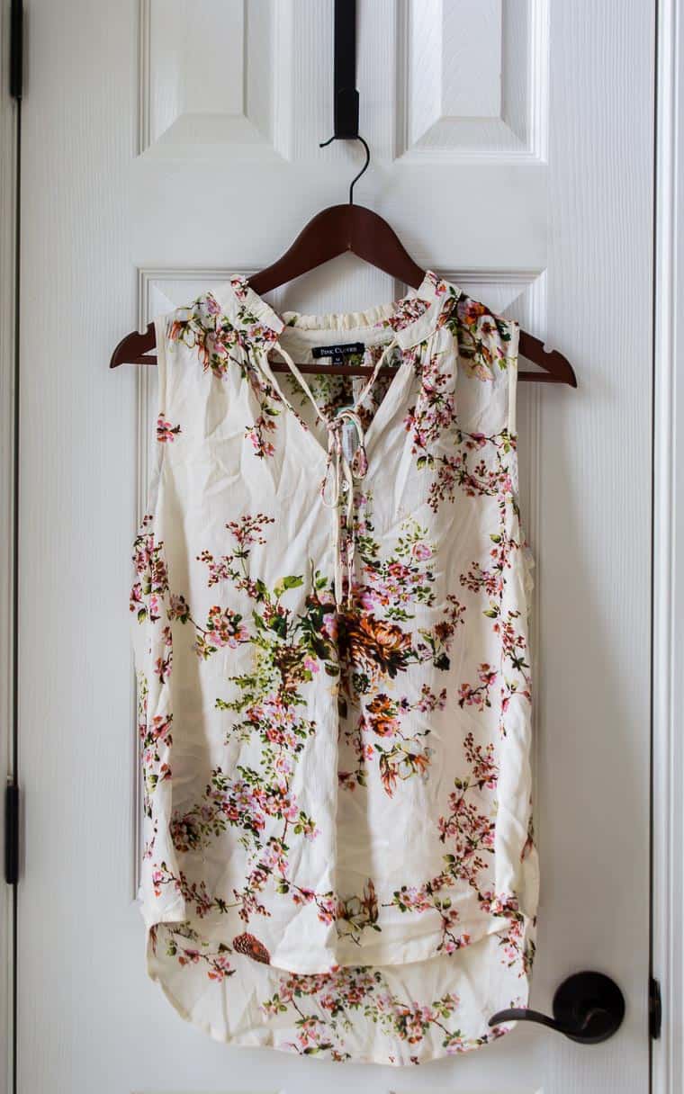 Stitch Fix Pink Clover Mahalo Tie Neck Top in cream with a floral design on a hanger over a white door