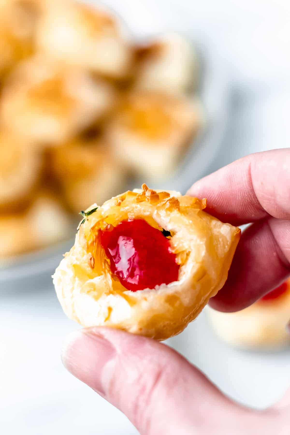 A single Gruyere cheese puff being held up over a plate of more cheese puffs.