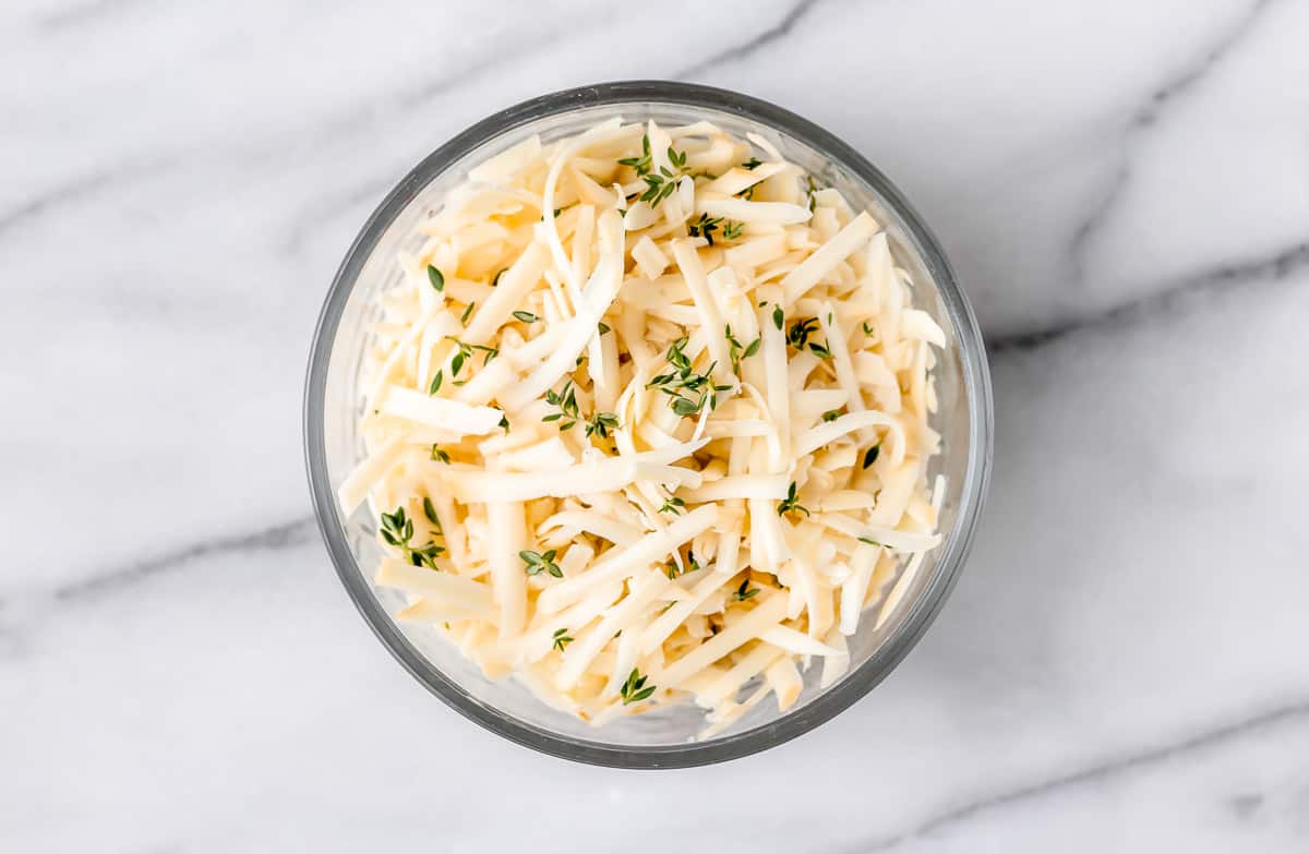 Shredded cheese and thyme in a bowl on a marble background.