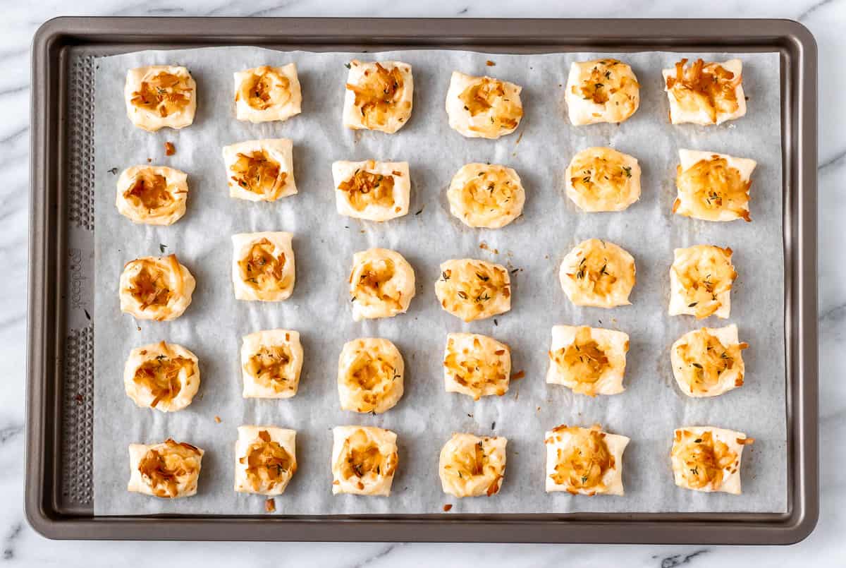 Baked puff pastry cheese puffs on a parchment paper lined baking sheet.