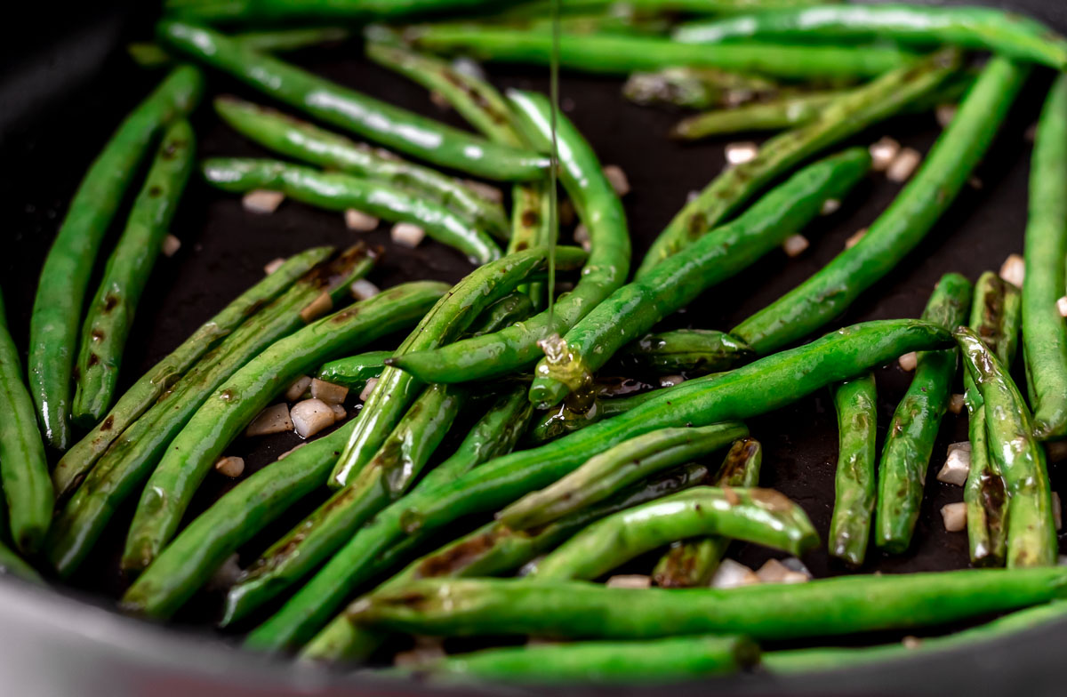 Close up of honey being drizzled onto green beans in a pan.