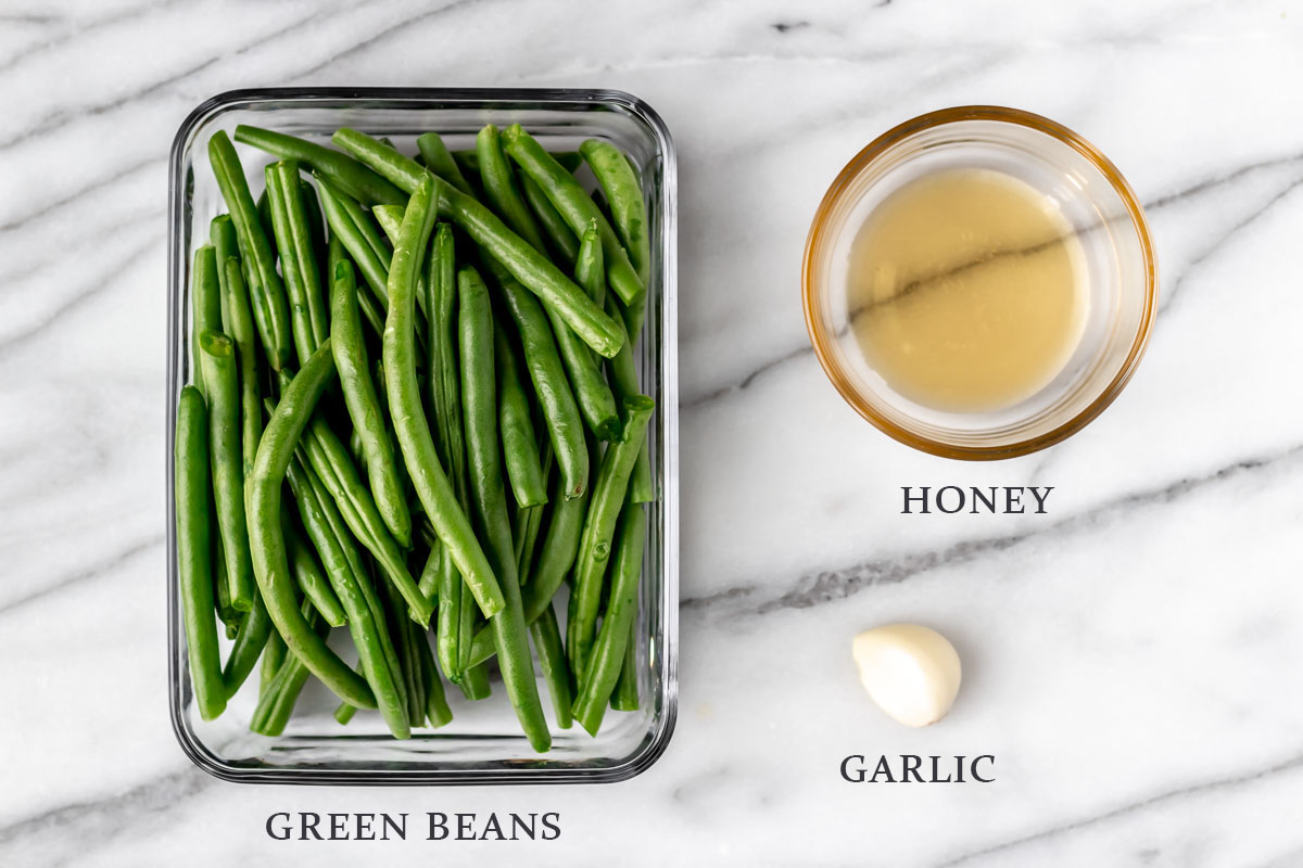 Ingredients to make honey garlic green beans on a marble background with text overlay.