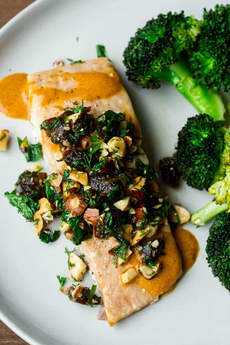 Roasted salmon topped with tapenade and a side of broccoli on a white plate over a wood backdrop