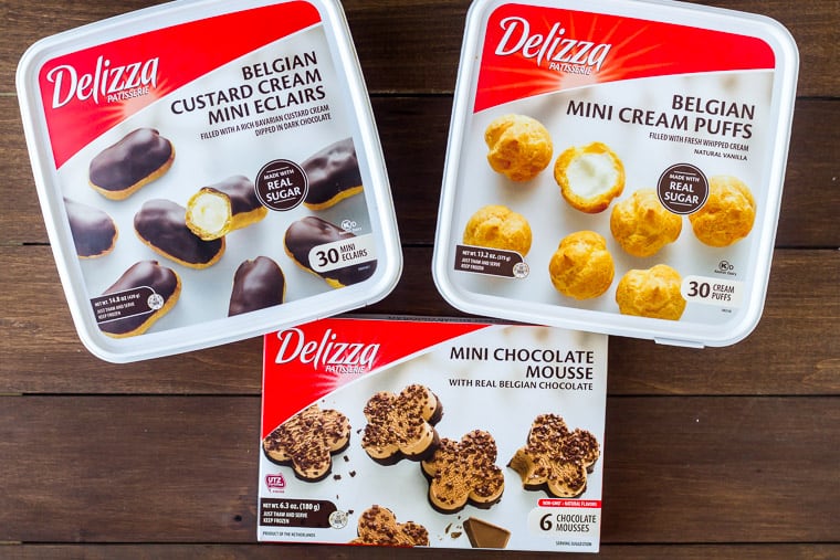 3 boxes of Delizza desserts including cream puffs, eclairs and mousse on a wood backdrop