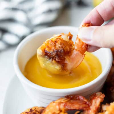 A coconut shrimp being dipped into a bowl o sweet mango dipping sauce.