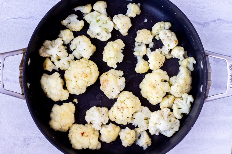 Cauliflower cooking in a black skillet over a white background