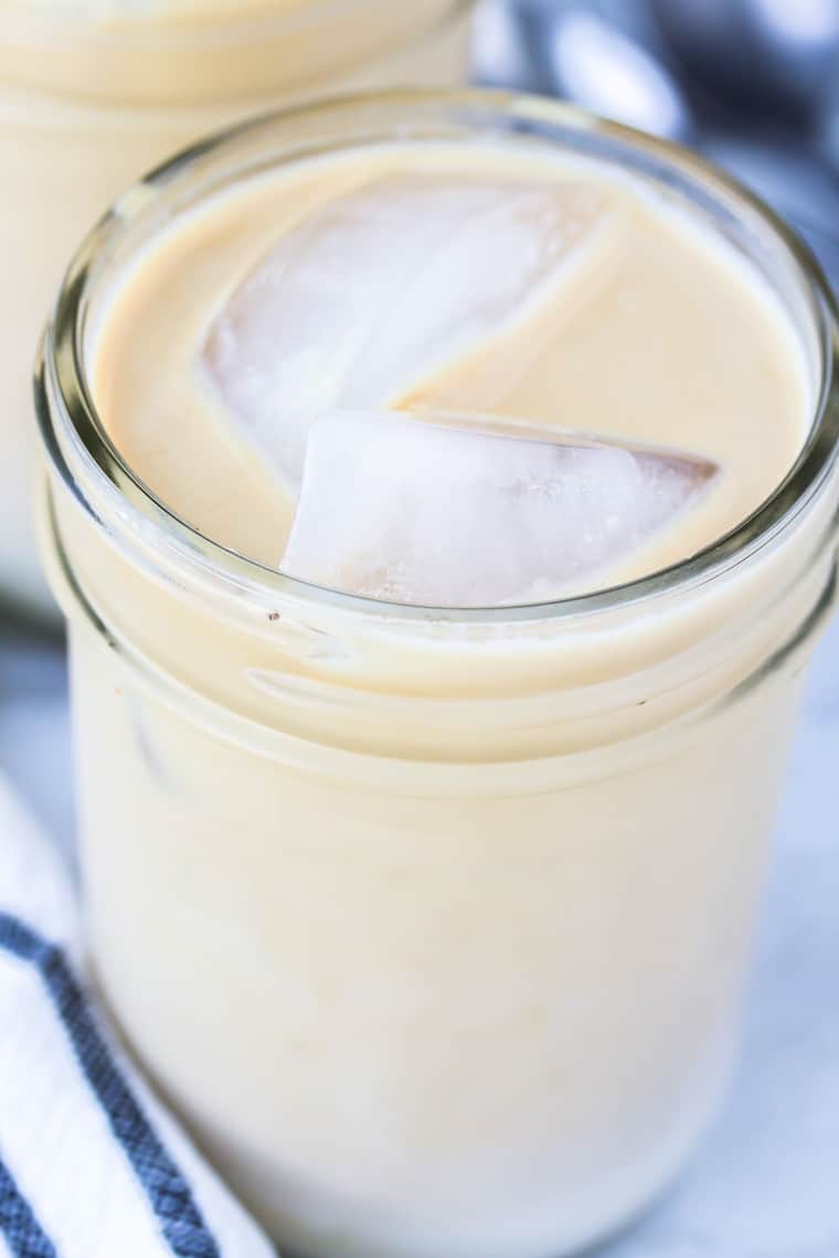 A close up of an Iced Vanilla Latte in a mason jar with a spoon and black and white napkin in the background