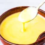Hollandaise Sauce in a dark orange bowl with a spoon over a white background