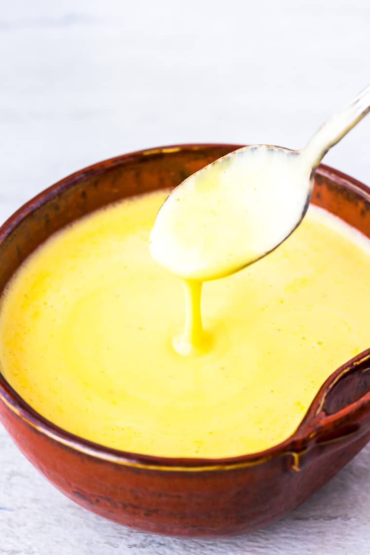 Hollandaise Sauce in a dark orange bowl with a spoon over a white background
