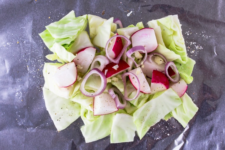 Cabbage, radishes, shallot, garlic, salt, and pepper on a sheet of foil.