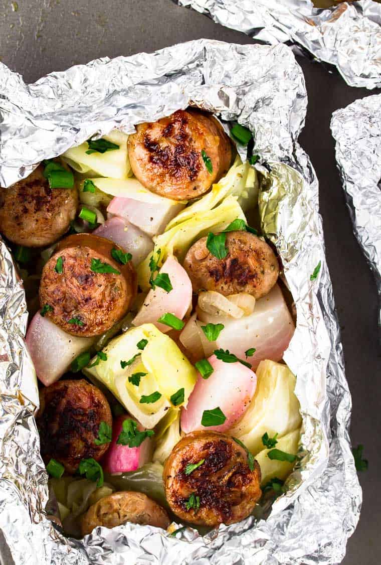 Sausage and cabbage foil packets with radishes close up on a baking sheet