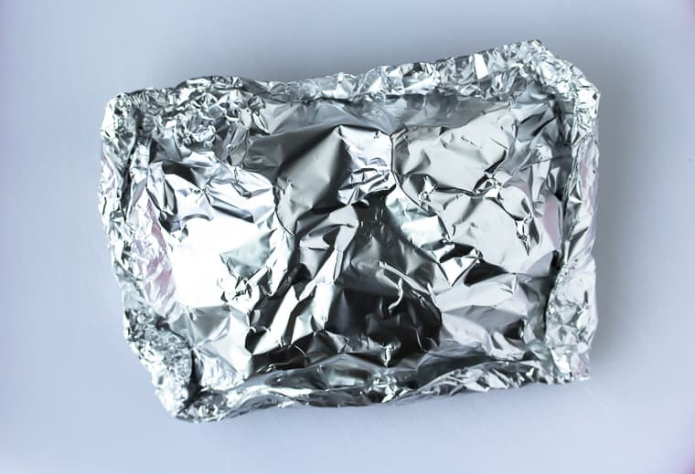 Foil packets all wrapped up and ready to be baked or grilled on a white background
