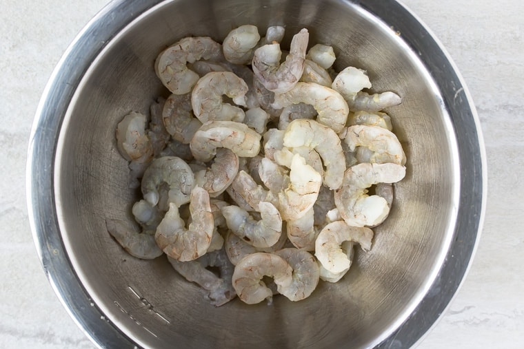 raw shrimp in a silver bowl over a white backdrop