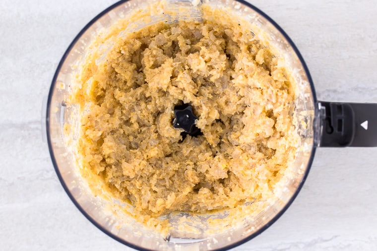 Shrimp cake mixture in food processor bowl over a white backdrop