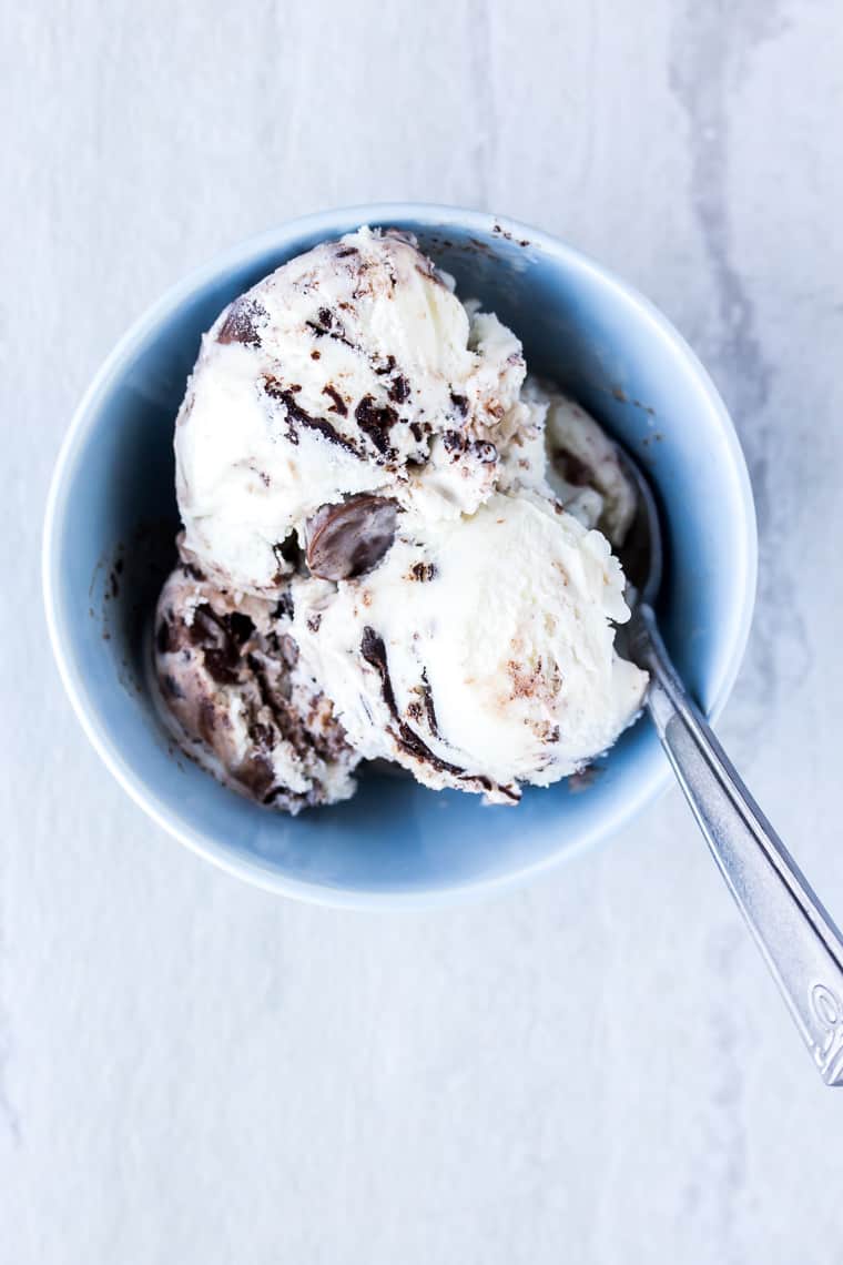 A Small light blue bowl of chocolate and vanilla Moose Tracks ice cream with a spoon in it on a white and gray backdrop