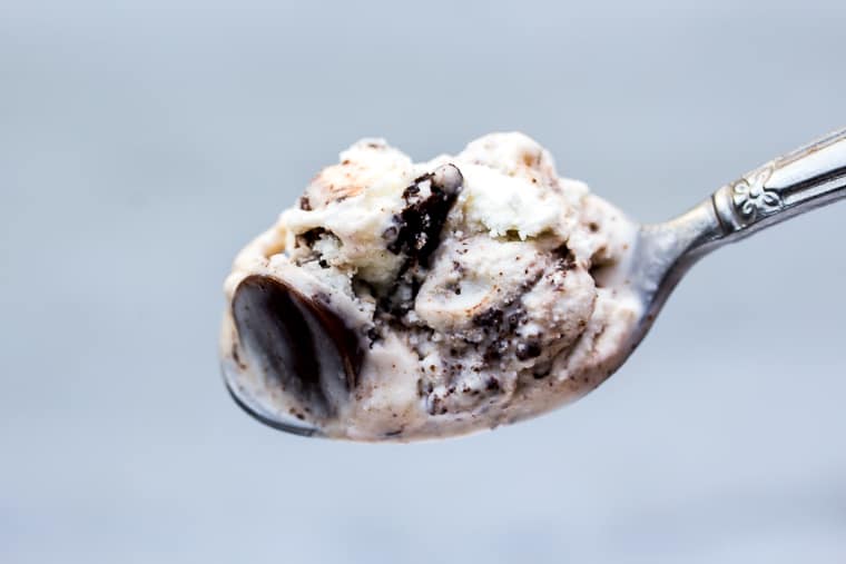 A close up of a spoonful of Moose Tracks ice cream that's vanilla with fudge and candy in it on a white background