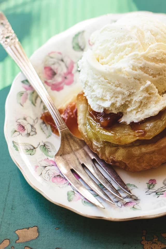 Close up on an apple tarte tatin on a floral plate with a fork and topped with ice cream