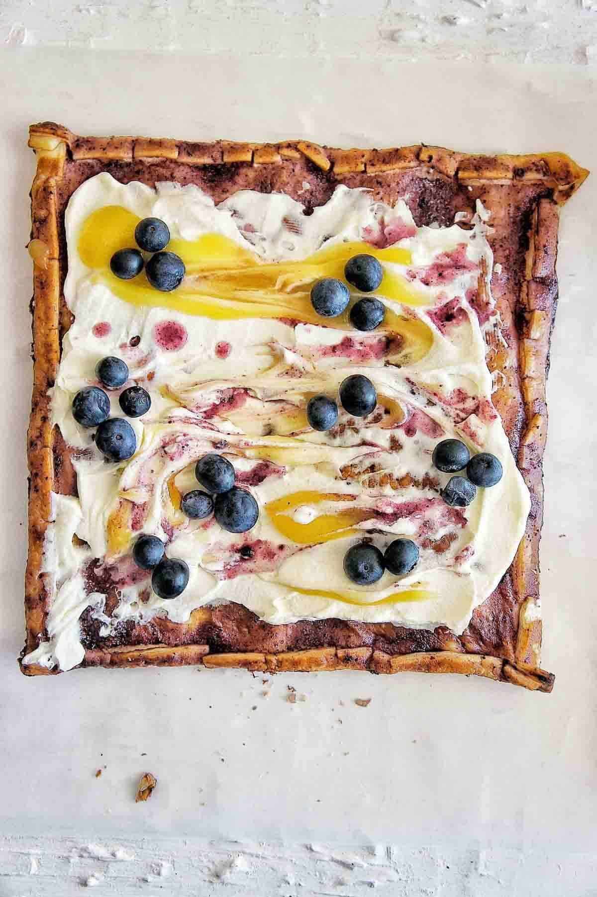 A puff pastry tart covered in blueberries, lemon curd, and cream on a white backdrop