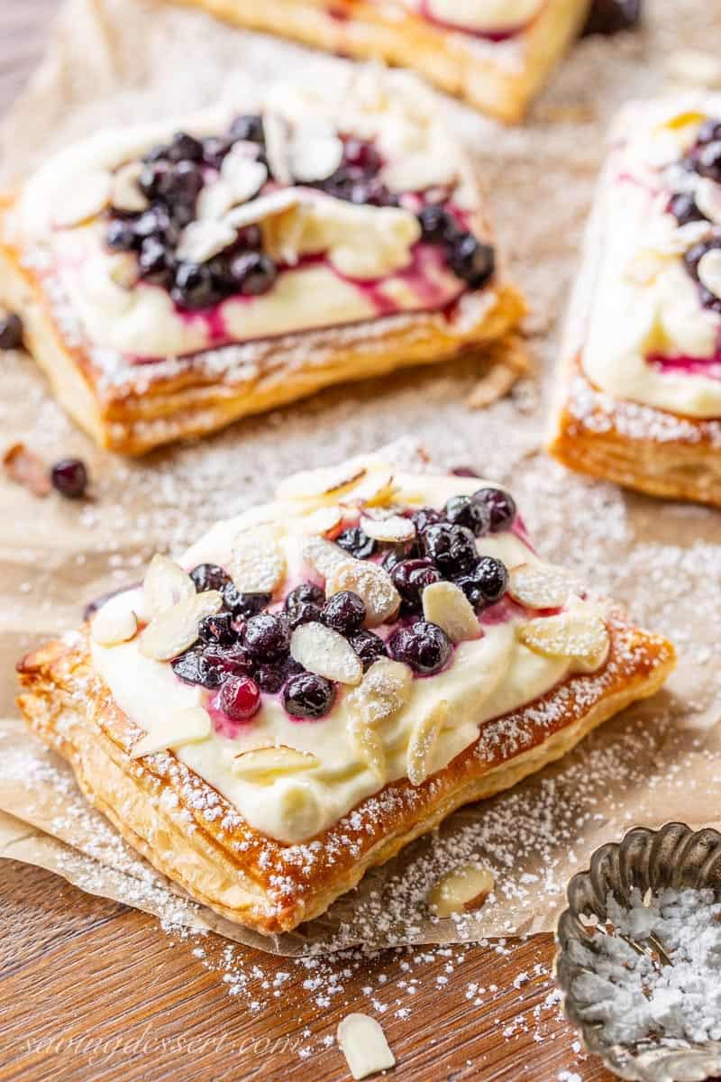 Blueberry Puff Pastry Tarts spread out on parchment paper and covered in powdered sugar 