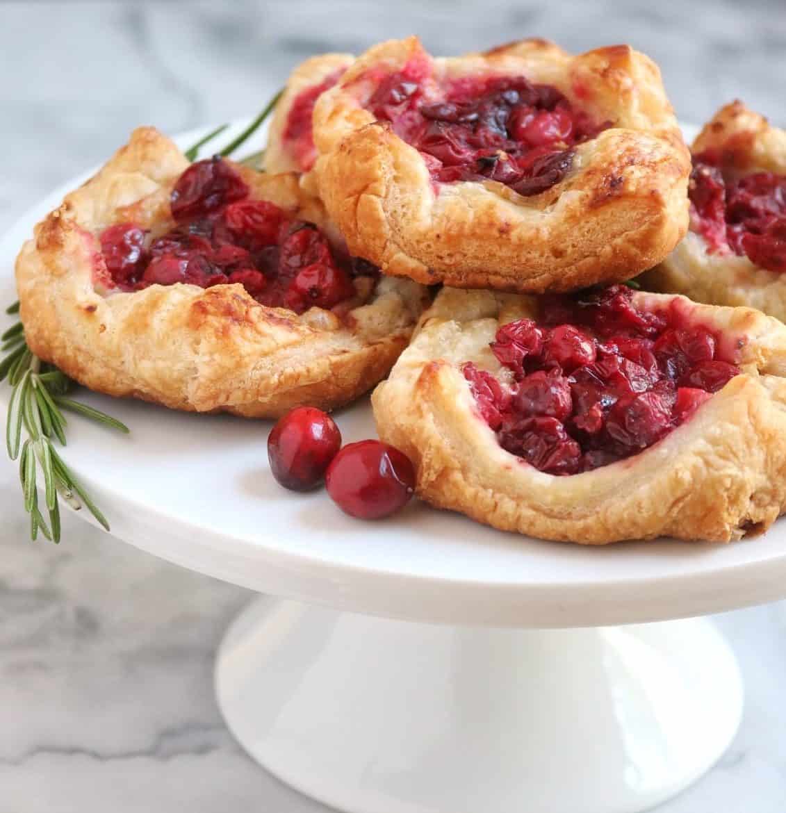 Cranberry Brie Tarts on a white cake platter with rosemary and fresh cranberries on a marble backdrop