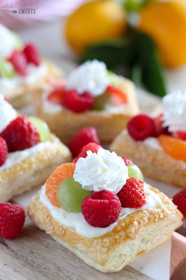 A white tray with mini cream cheese fruit tarts with lemons in the background