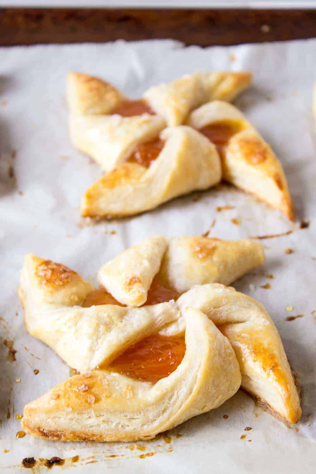 Close up of 2 puff pastry pinwheels filled with jam on a piece of parchment paper