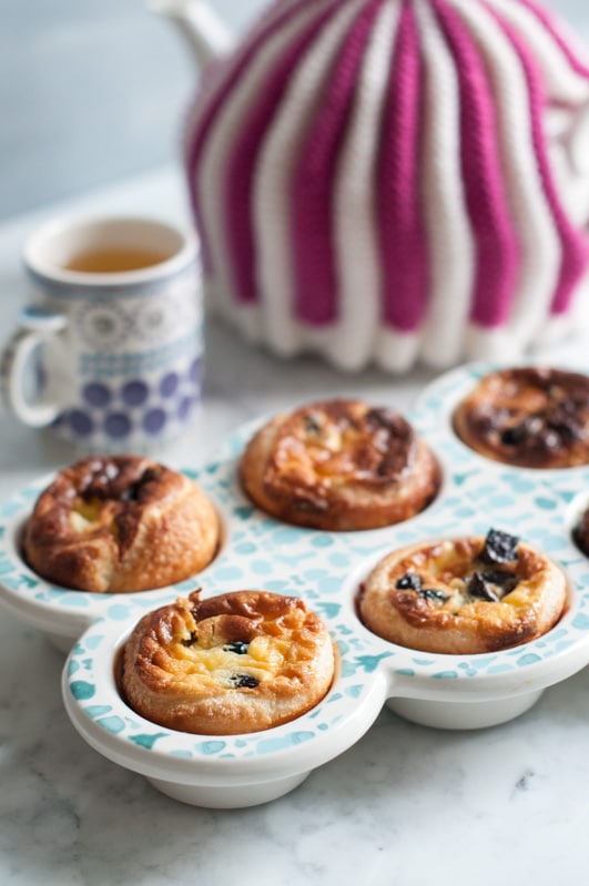 Custard Tarts with Prunes in a Baking Dish with a cup of tea and purple and white striped tea pot in the background