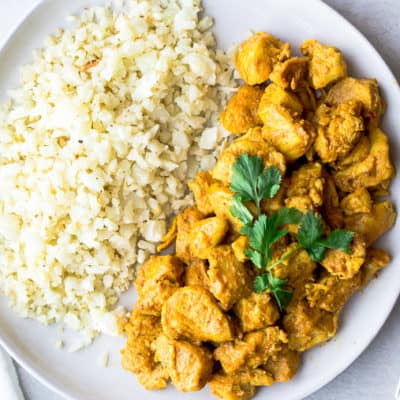 Curry Chicken on a white plate with cauliflower rice and a fork and white napkin off to the sides