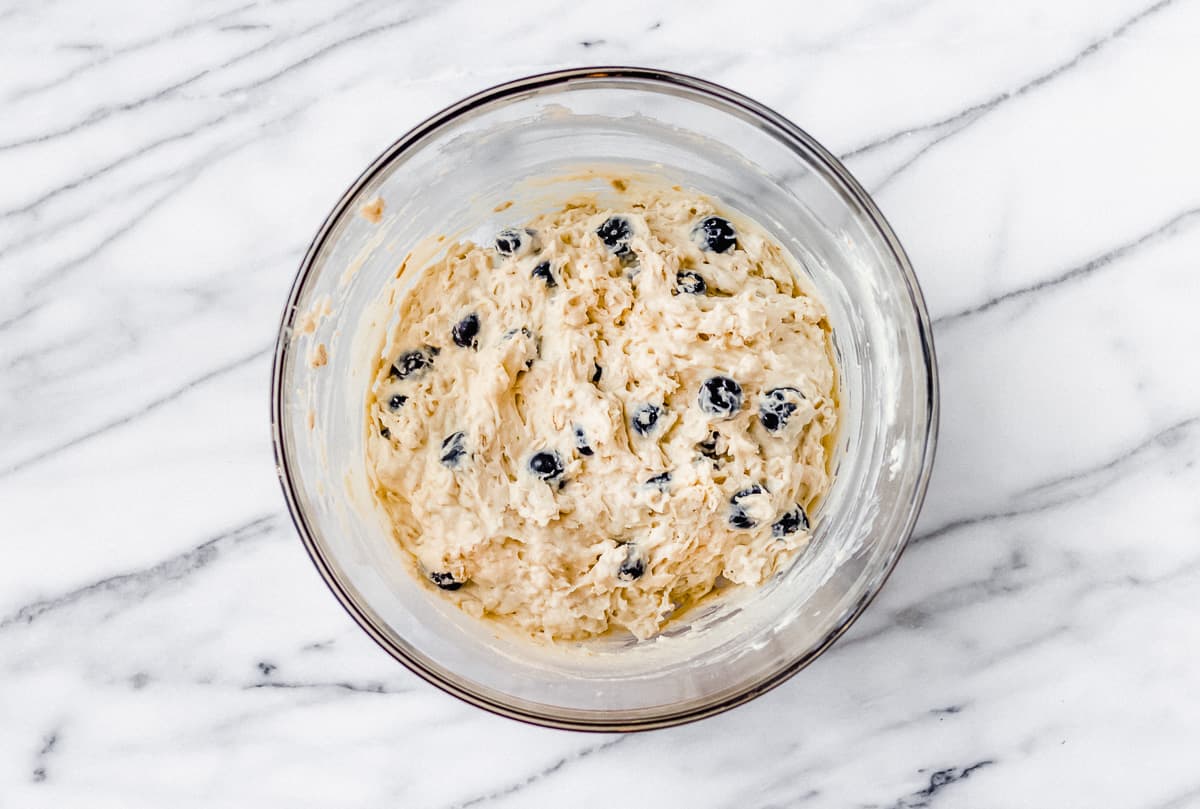 Blueberry oat muffin batter in a glass bowl on a marble backdrop