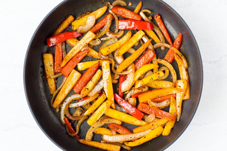 Peppers and onion cooking in a black skillet over a white background