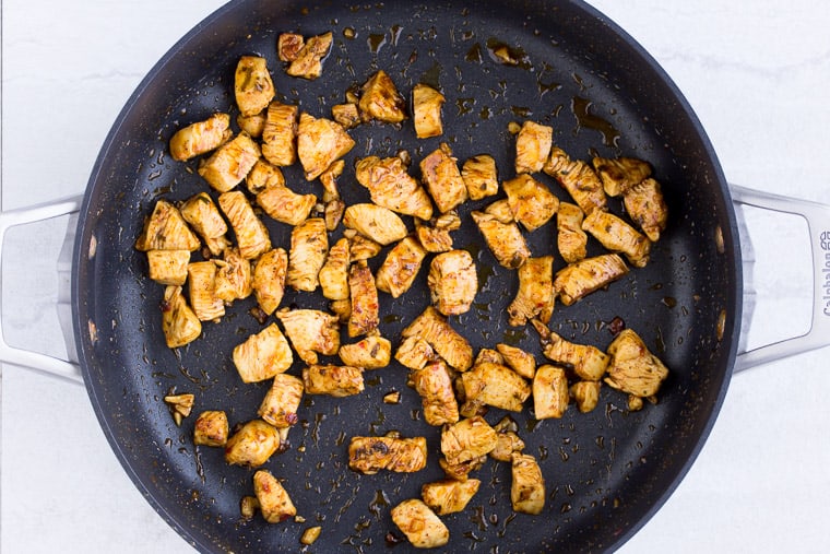 Seasoned chicken cooking in a block skillet over a white background
