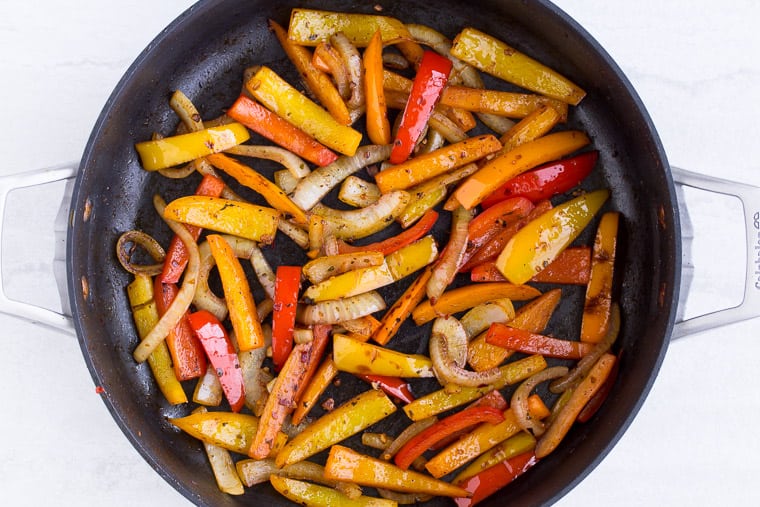 Peppers and onions cooking in a black skillet over a white background
