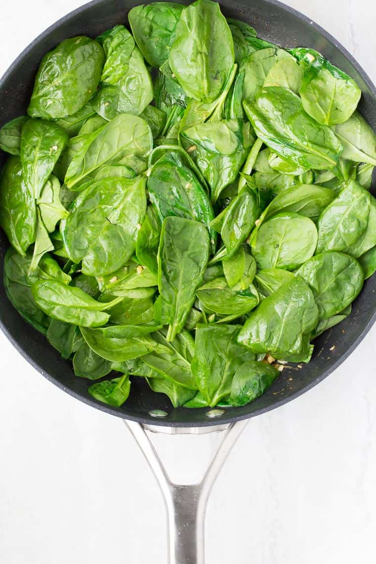 Spinach in a black skillet over a white background