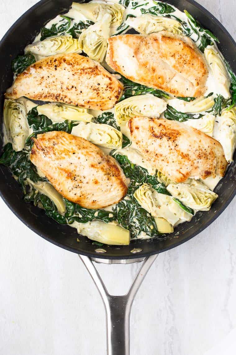 Chicken, spinach and artichokes in a black skillet on a white background
