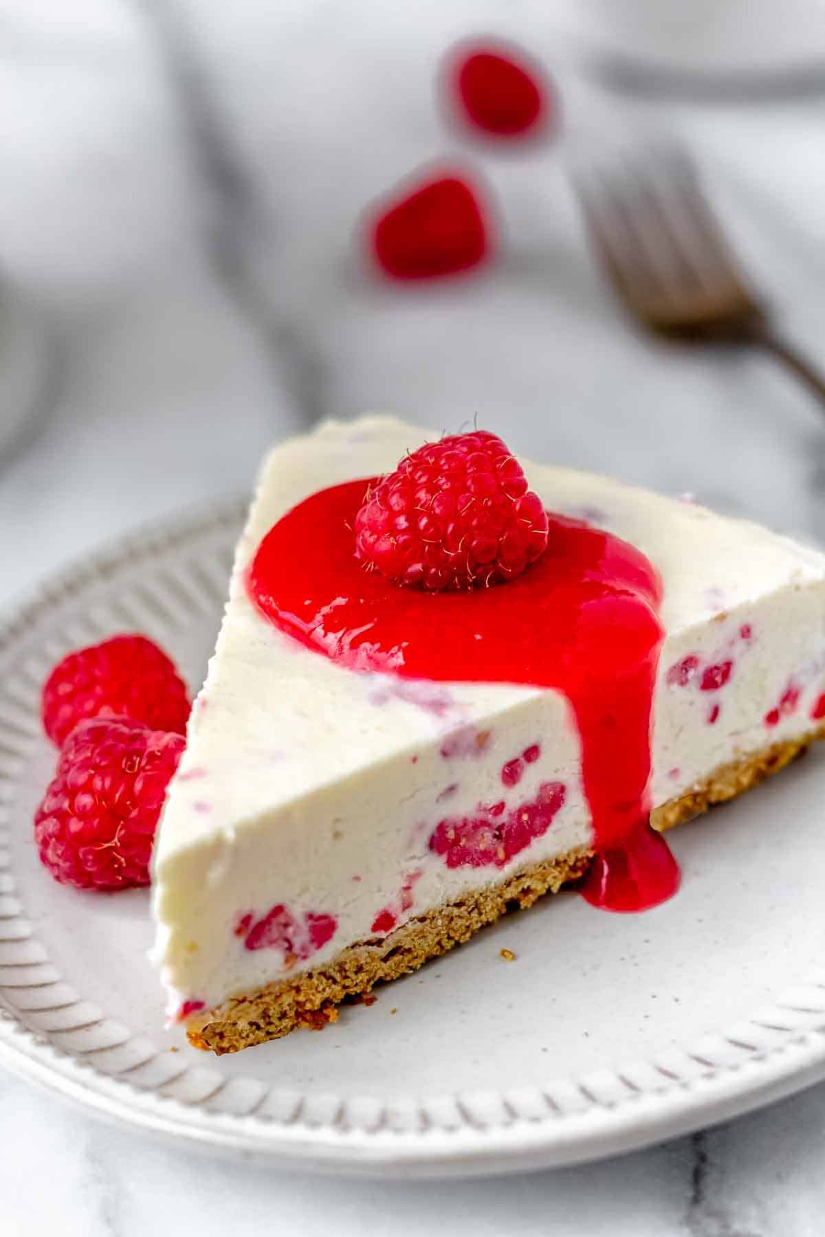 A slice of no-bake raspberry cheesecake with a fork and fresh raspberries in the background.