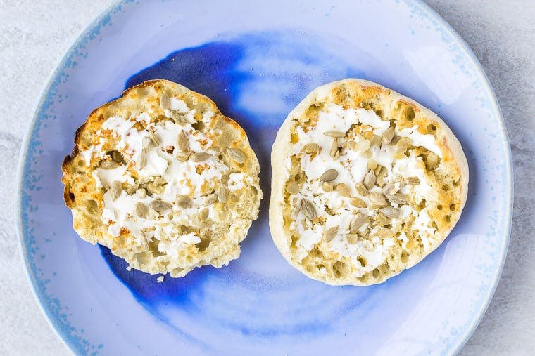 English muffin halves with cream cheese on a blue plate over a white background