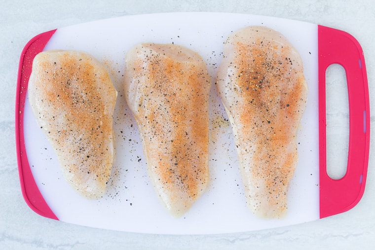 3 pieces of seasoned chicken on a white cutting board