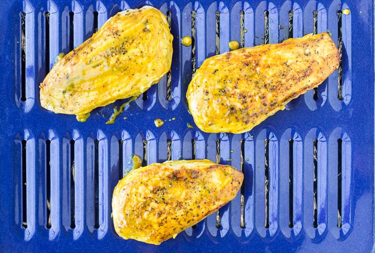Chicken breasts on a blue broiler pan brushed with mustard sauce