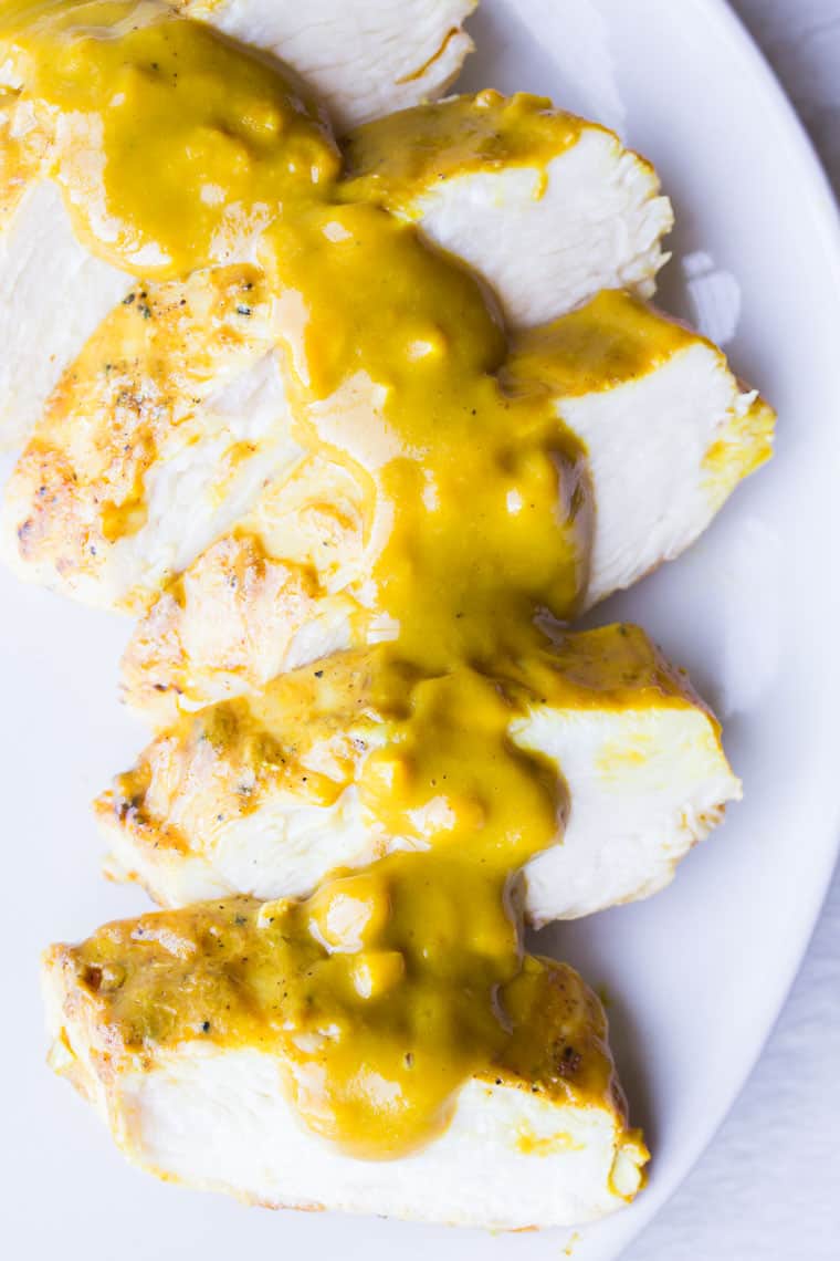 Grilled Mustard Chicken sliced and topped with mustard sauce on a white plate